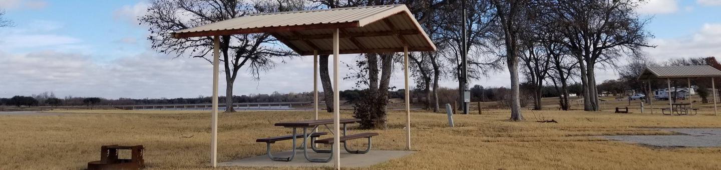 View of Site 39S, highlighting covered picnic table, shade trees, and fire ring.