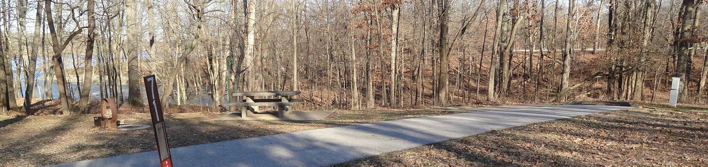 This site is located near the waters edge providing a great view. This electricity hook up is on the right side of the paved parking/camping pad. The picnic table and fire pit are on the right side of the pad. There are also plenty of trees providing shade. 